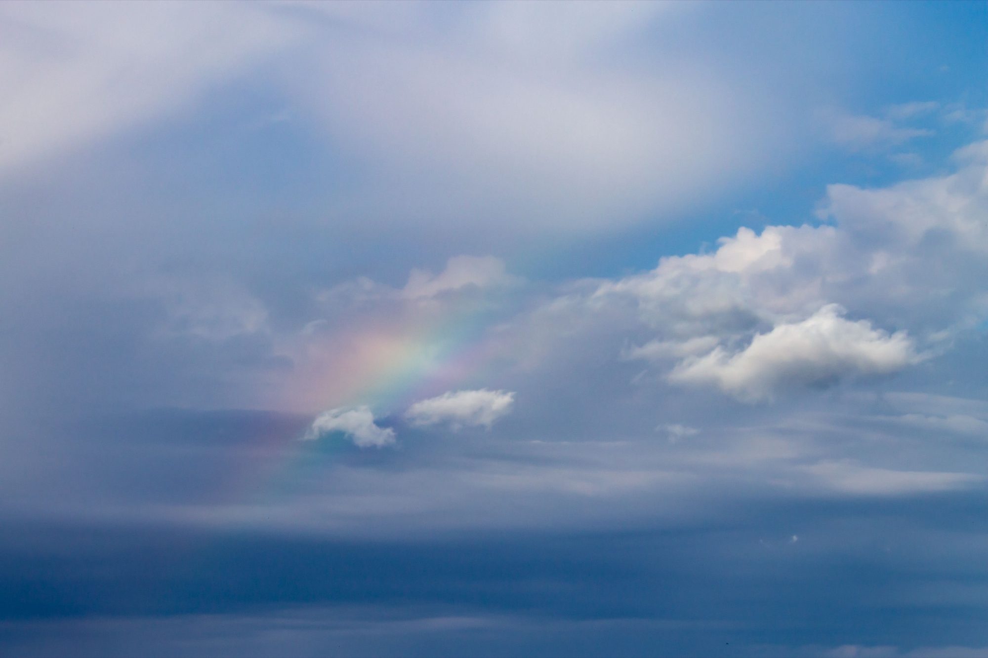 A faint rainbow glowing softly among clouds over the ocean