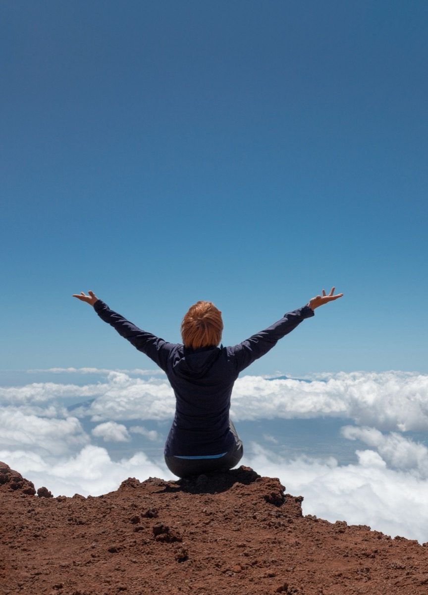 A woman kneeling with her arms raised above a sea of clouds